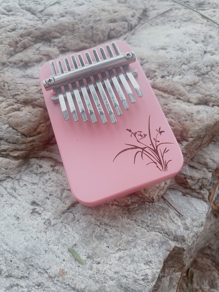 Pink 10 key kalimba with floral engraving resting on stone surface, easy instrument for beginners